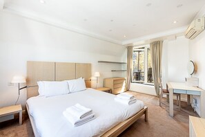 Ein Hotelzimmer mit Bett, Nachttischen, Schreibtisch, Stuhl und einem Vorhangfenster.