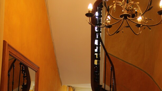 A grand staircase with a chandelier, a mirror reflecting the staircase, and a door at the top.