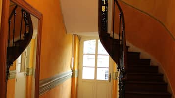 Un magnifique escalier orné d’un lustre, un miroir qui reflète l’escalier, et une porte en haut.