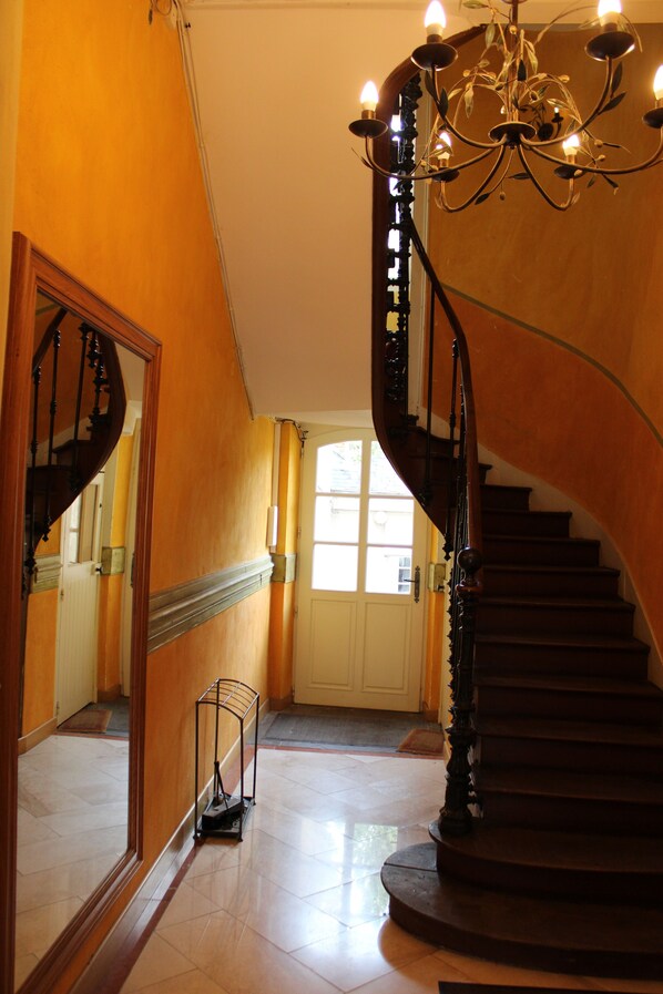 A grand staircase with a chandelier, a mirror reflecting the staircase, and a door at the top.