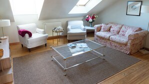 A loft-style room with a glass coffee table, white armchairs, a floral sofa, and a skylight.