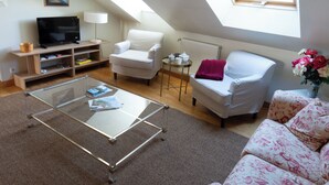 A living room with a TV, white armchairs, a glass coffee table, and a skylight.