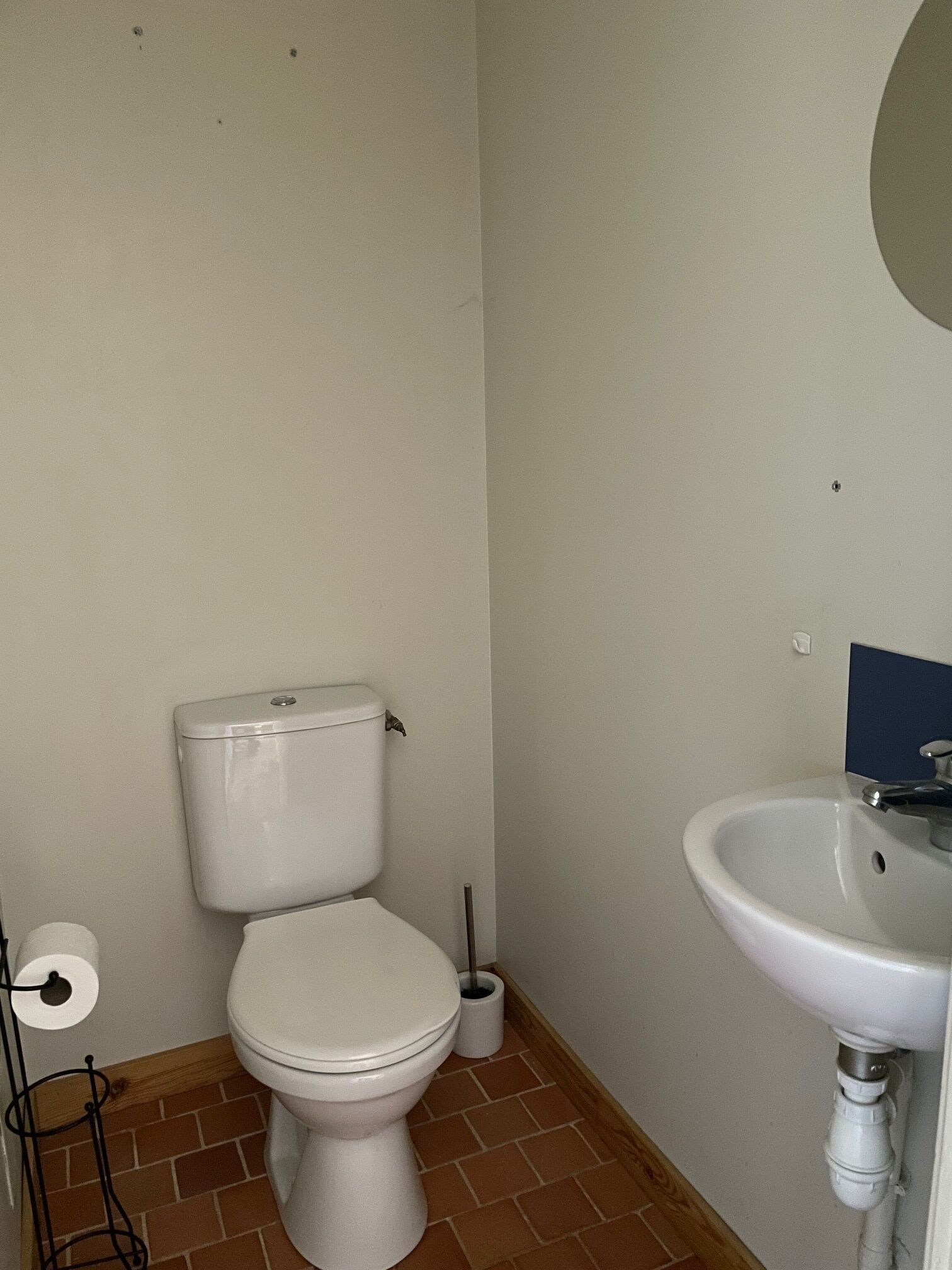 Un baño pequeño con inodoro, lavamanos y un rollo de papel higiénico.