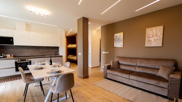 Eine moderne Küche mit weißen Schränken, einem Esstisch für vier Personen und einem braunen Sofa im Wohnbereich.