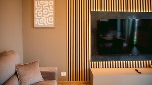 Ein Wohnzimmer mit einem an der Wand montierten Flachbildfernseher, einer Couch mit Kissen und einem gerahmten abstrakten Kunstwerk.