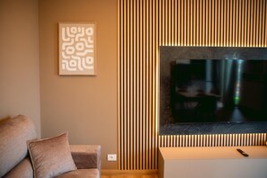 En stue med et fladskærms-TV monteret på væggen, en sofa med puder og et indrammet abstrakt kunstværk.