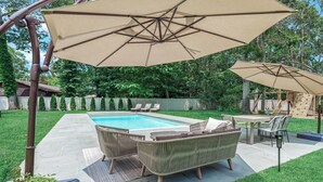 Een achtertuin met een zwembad, tuinmeubilair en parasols.