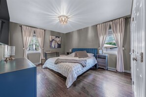 A bedroom with a bed, bedside tables, a lamp, a painting, and a view of the outdoors. - Summer Retreat: Private Jacuzzi, Game room & more (Centereach)