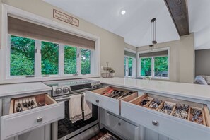 A kitchen with a built-in oven, a stovetop, and a large window with a view of greenery. - Summer Retreat: Private Jacuzzi, Game room & more (Centereach)
