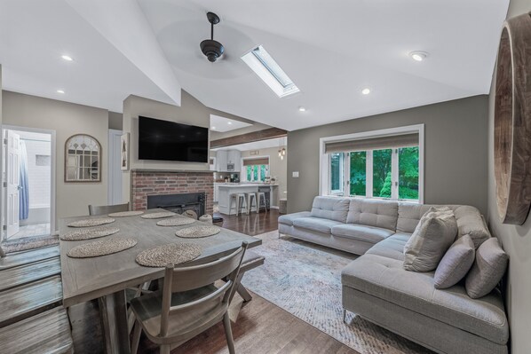 A spacious living area with a dining table, sofa, and kitchen in the background. - Summer Retreat: Private Jacuzzi, Game room & more (Centereach)