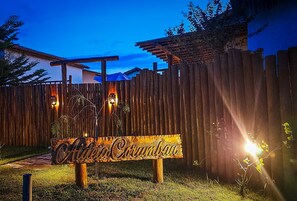 Uma placa de madeira com o texto 'Aldea Corubán' em ambiente rústico ao ar livre ao entardecer.