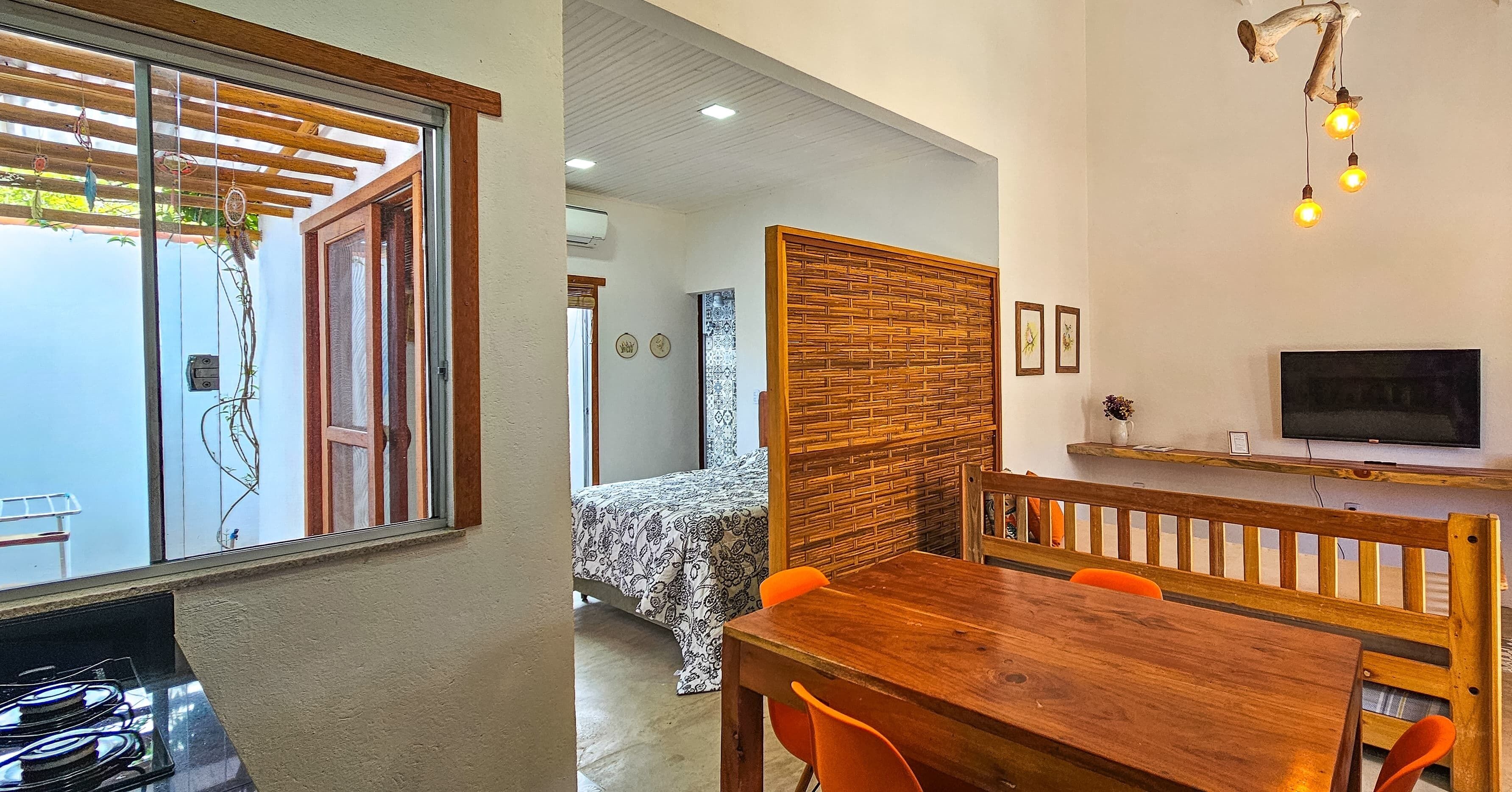 Quarto com cama, uma mesa de jantar de madeira com cadeiras, televisão e janela com vista para o exterior.
