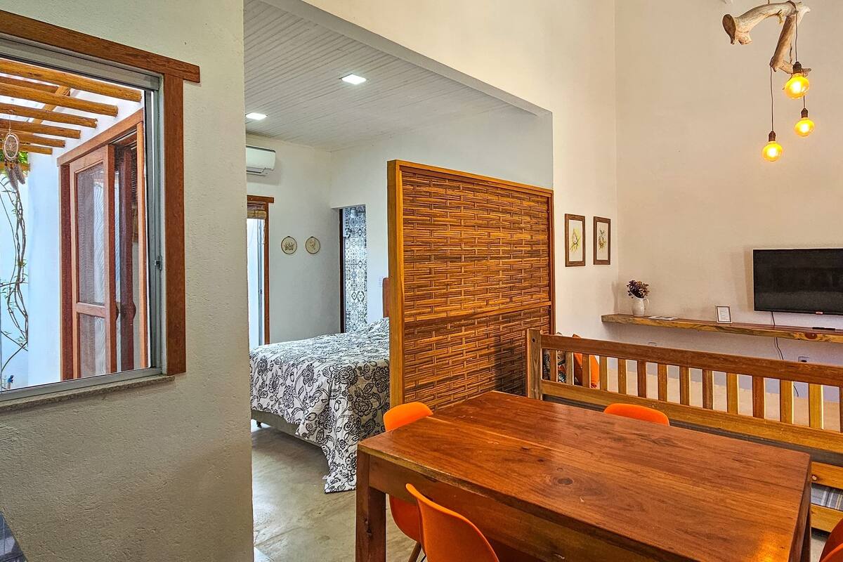 A room with a bed, a wooden dining table with chairs, a TV, and a window with a view of the outside.