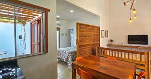 Quarto com cama, uma mesa de jantar de madeira com cadeiras, televisão e janela com vista para o exterior.