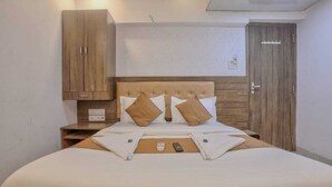 A neatly made bed with a wooden headboard, a nightstand with a remote control, and a wardrobe with a wooden finish. - Hotel Sonal Inn (Mumbai)