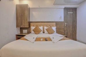 Ein ordentlich bezogenes Bett mit Holz Kopfteil, ein Nachttisch mit Fernbedienung und ein Schrank mit Holzoptik.