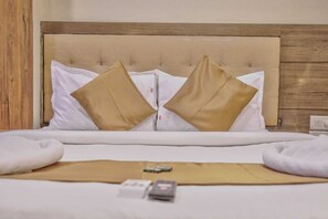 A neatly made bed with white and beige pillows, a remote control, and a small item on the bed.