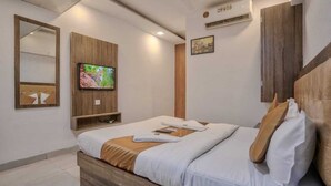 A modern hotel room with a bed, a TV mounted on the wall, a wooden headboard, and a mirror. - Hotel Sonal Inn (Mumbai)