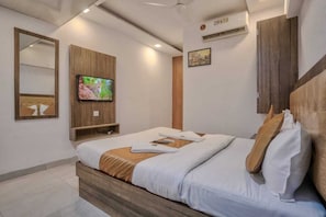 A modern hotel room with a bed, a TV mounted on the wall, a wooden headboard, and a mirror. - Hotel Sonal Inn (Mumbai)