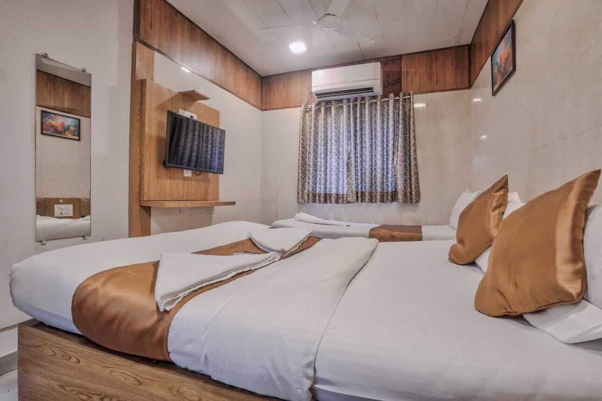 Ett hotellrum med två sängar, en platt-TV, en luftkonditioneringsanläggning och ett fönster med mönstrade gardiner.