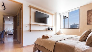 Un dormitorio moderno con cama, televisor montado y ventana con vista a la ciudad.