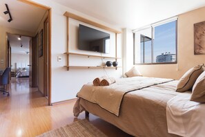 Ein modernes Schlafzimmer mit einem Bett, einem an der Wand befestigten Fernseher und einem Fenster mit Blick auf die Stadt.