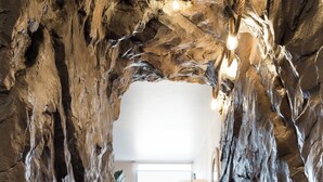 Un pasillo con pared de roca natural, suelo de madera y una lámpara.