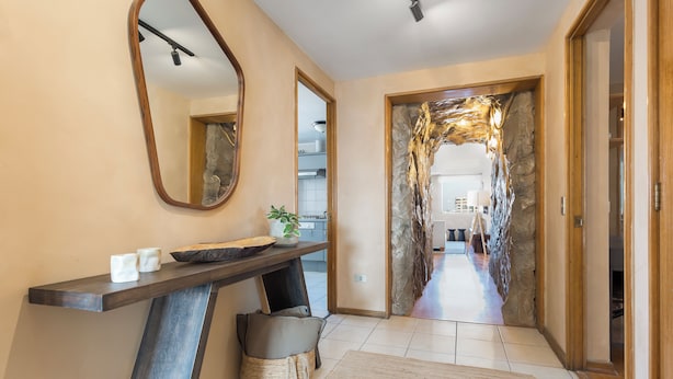 Un pasillo moderno con una pared de piedra, una consola de madera, un espejo y una cesta.