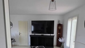 Un salon avec un canapé noir, un téléviseur à écran plat, un meuble en bois et une plante en pot.