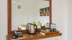 Habitación de hotel con un escritorio de madera, un teléfono, una tetera, una bandeja con botellas de agua y una cama con almohadas verdes.