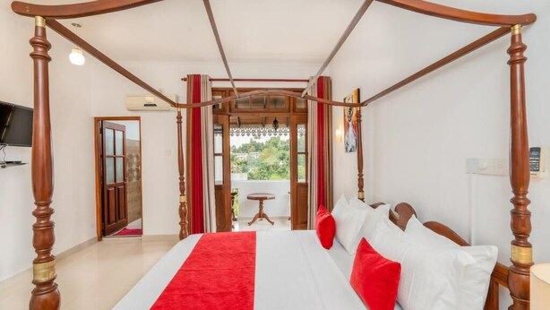 Una cama con dosel, con un corredor rojo, sábanas blancas y almohadas rojas.