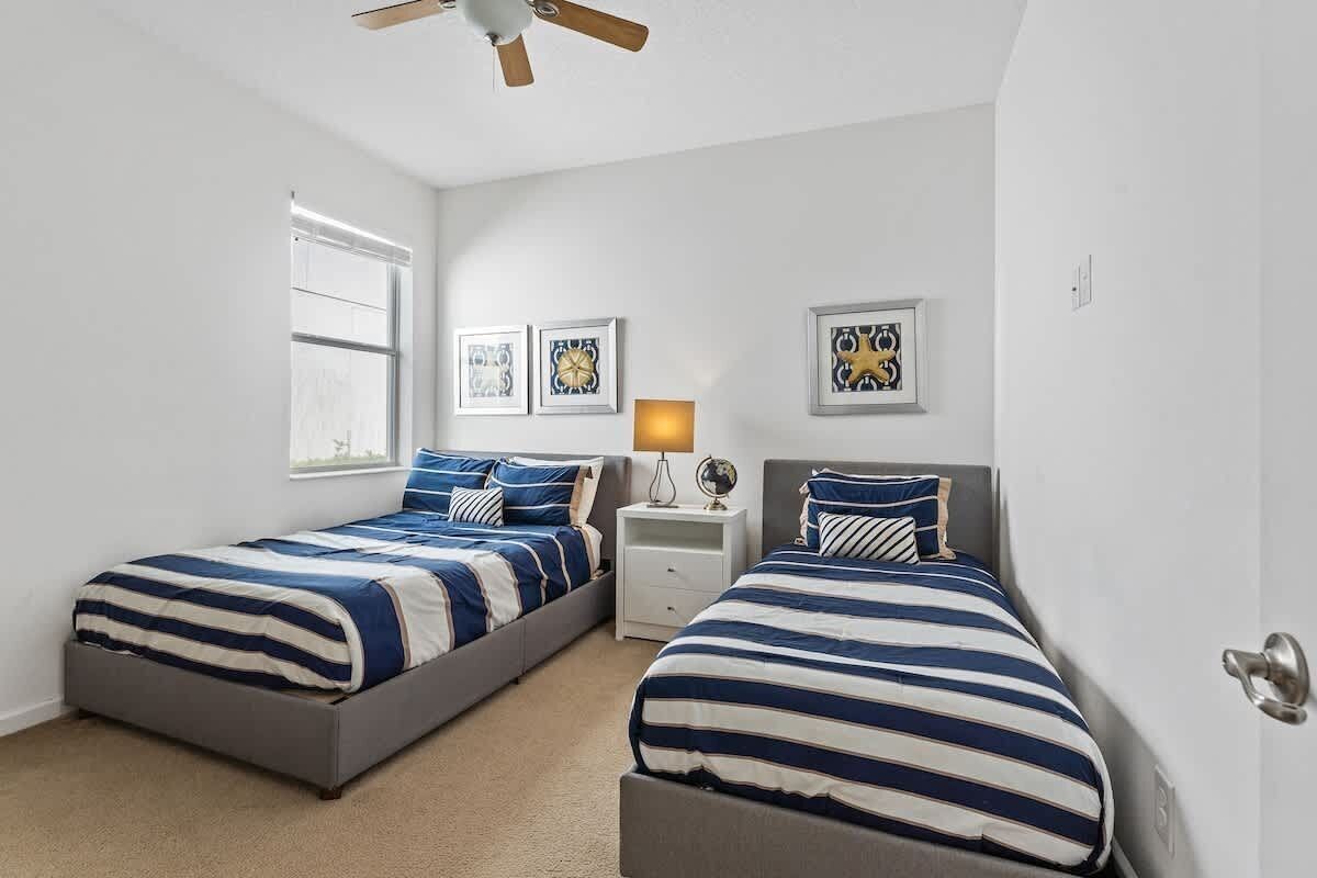 A bedroom with two beds, a ceiling fan, a window, and wall art.
