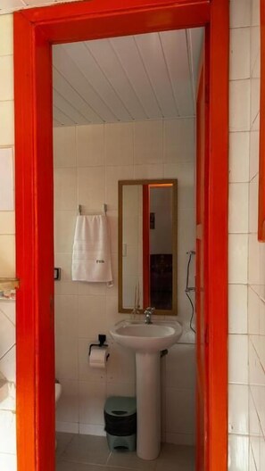 Un baño con un lavamanos blanco, un espejo, una toalla colgada en la pared y un cubo de basura.