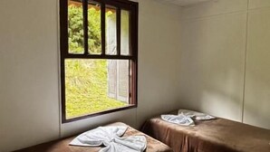 Une chambre avec deux lits simples, une fenêtre avec des stores et un luminaire au plafond.