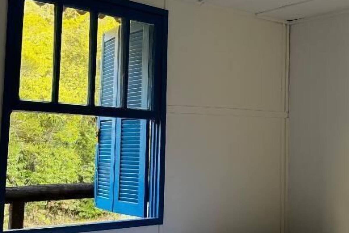 Un dormitorio con una cama, una ventana con persianas azules y vistas al verdor exterior.