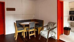 Une pièce avec un plancher en bois, une table à manger avec des chaises, un fauteuil à motifs et une porte rouge.