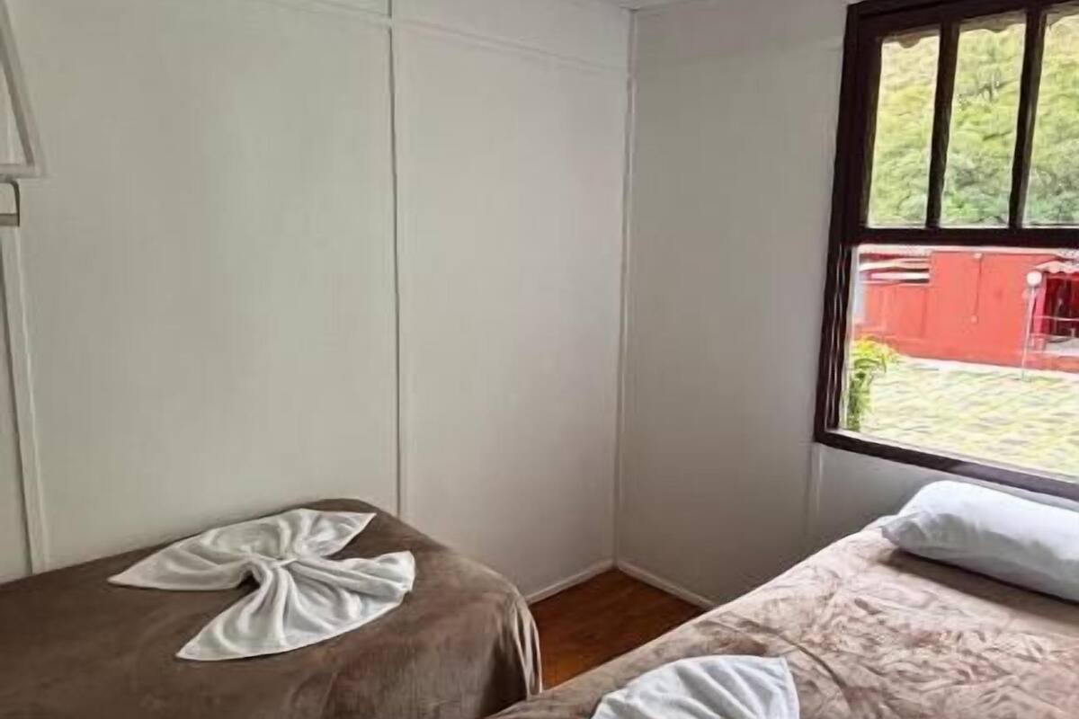 Habitación con dos camas, cada una con una toalla encima. Se ve un edificio rojo a través de la ventana.