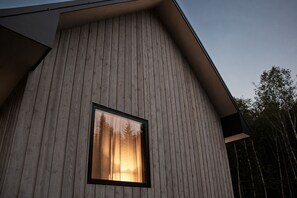 En moderne bygning med lodrette træfacader, et vindue der viser udsigt til træer, og et skråt tag.