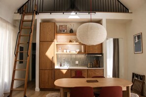 Eine moderne Küche mit Holzausbau, einem Esstisch mit Stühlen, einer Pendelleuchte und einer Holzleiter.