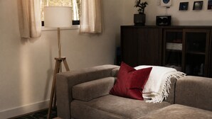 Un salon comprenant un canapé, une lampe sur pied, une table basse en bois et un meuble avec des tableaux encadrés.