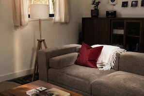 Ein Wohnzimmer mit einer Couch, einer Stehlampe, einem Holztisch und einer Kommode mit gerahmten Bildern.