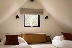 A bedroom with a sloped ceiling, a window with a view of trees, a wooden bench, and two bedside tables with lamps. - Forest retreat near Olympic National Park with fire pit (Port Angeles)