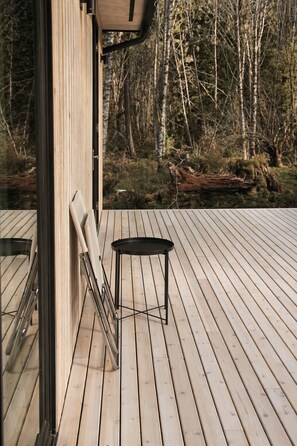 Eine Holzterrasse mit einem Metallstuhl und Tisch, mit Blick auf ein bewaldetes Gebiet.