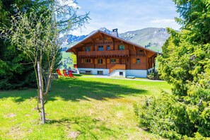 Un chalet en bois doté d’un balcon, entouré de verdure et de montagnes.
