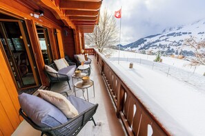 Een houten terras met buitenmeubilair, een vlag en een besneeuwd berglandschap.