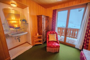 Een houten interieur met een wastafel, een stoel, een kast en een zicht op een besneeerd landschap door een raam.