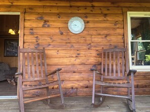 Zwei Holzstühle gegenüberliegend auf einer Veranda mit einer Holzwand und einer Uhr.