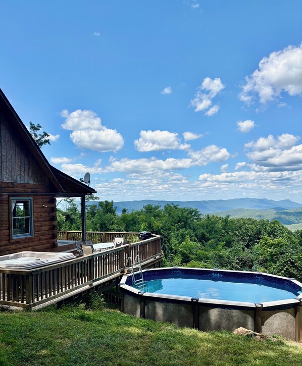 A wooden cabin with a deck, a hot tub, and a view of a mountainous landscape.