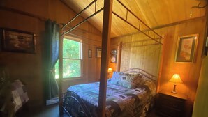 Un dormitorio con una cama con dosel, una mesita de noche con lámpara, un aparador y una ventana con cortinas.