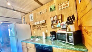 Una cocina con armarios de madera, un refrigerador, un lavavajillas, un microondas y una cafetera. Hay letreros en la pared, incluyendo uno que dice 'DON'T FEED THE BEARS'.